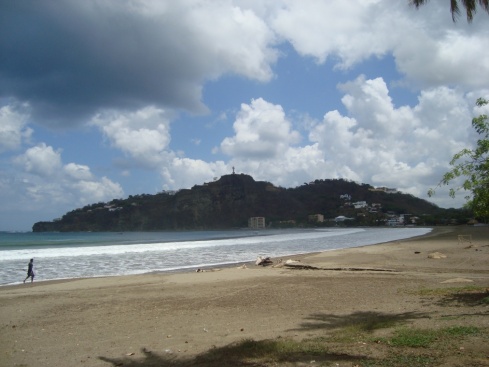The beach in the daytime. A statue of Jesus stands on the hill in the distance.